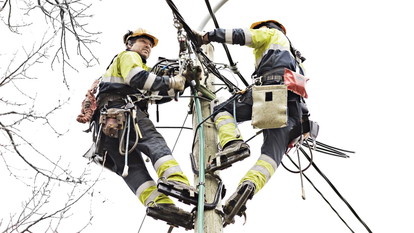 Bildet viser to personar i ei høyspentmast